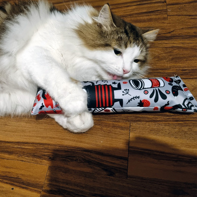 Liegende Katze umarmt Spielrolle aus der Crazy-Comic-Kollektion mit beiden Pfoten und leckt daran