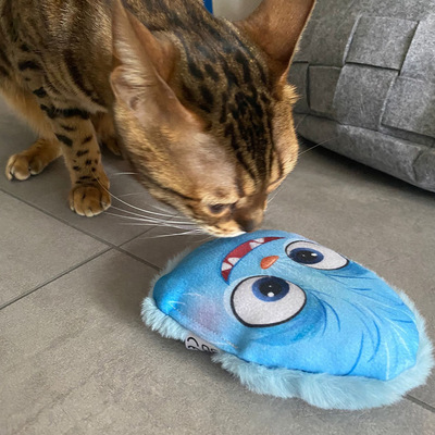 Katze schnuppert an Katzenkissen im Design blaues Monster