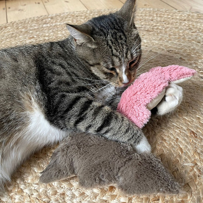 Liegende Katze hat zwei Plüschspielzeuge in Form von Tannenbäumen in den Pfoten