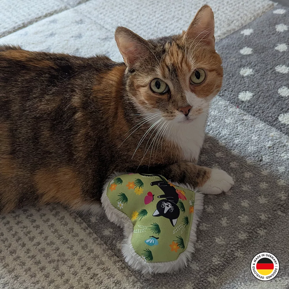 Katzenspielzeug in Form des Lucy-Plüschherzens liegt neben Katze
