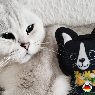 Katzenspielzeug in Form der Lucy-Katze lehnt sich an weißer liegender Katze an