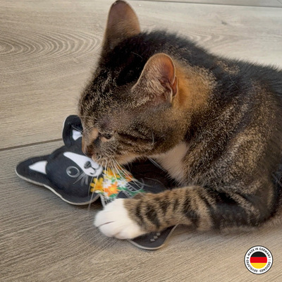Liegende getigerte Katze hält Katzenspielzeug in Form der Lucy-Katze mit der Pfote auf dem Boden fest