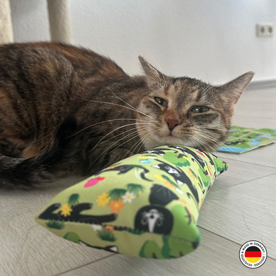Liegende Katze mit Kopf auf Katzen-Spielrolle aus Stoff, im Lucy-Design, Grundfarbe hellgrün mit schwarzer Katze und anderen Motiven